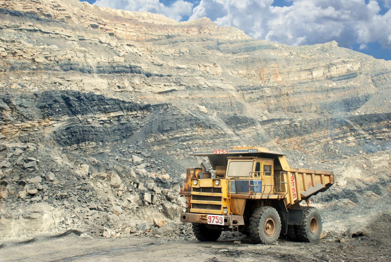 Home A large yellow mining truck in a rocky quarry under a clear sky.