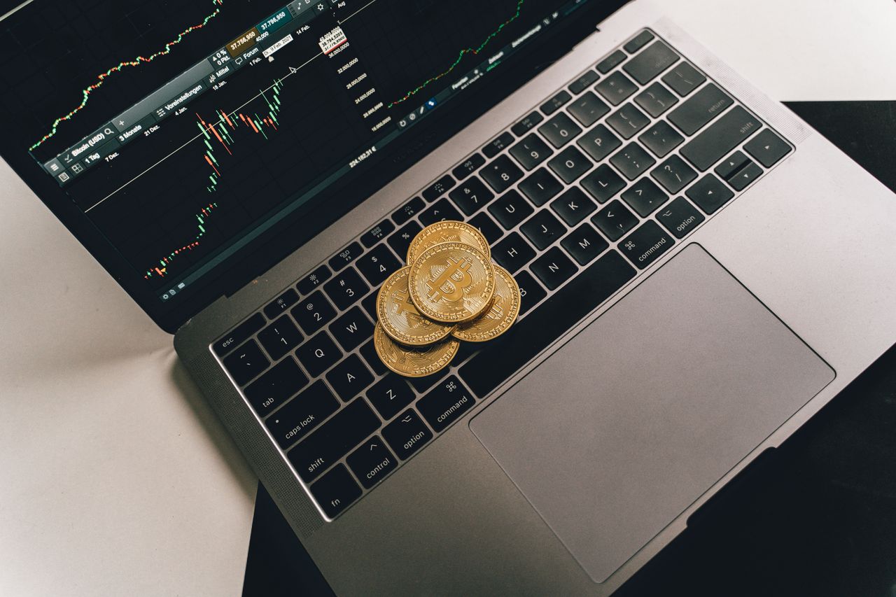 Home Bitcoin coins placed on a laptop keyboard while a trading chart displays on the screen, showcasing digital finance.